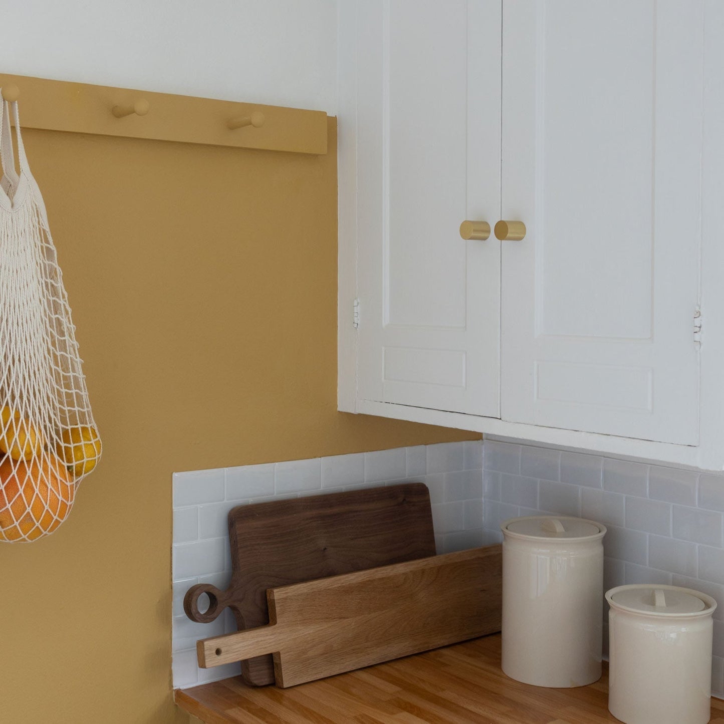 Front view of Cove Knob showcasing cylindrical brass-colored hardware on white cabinet doors in a kitchen