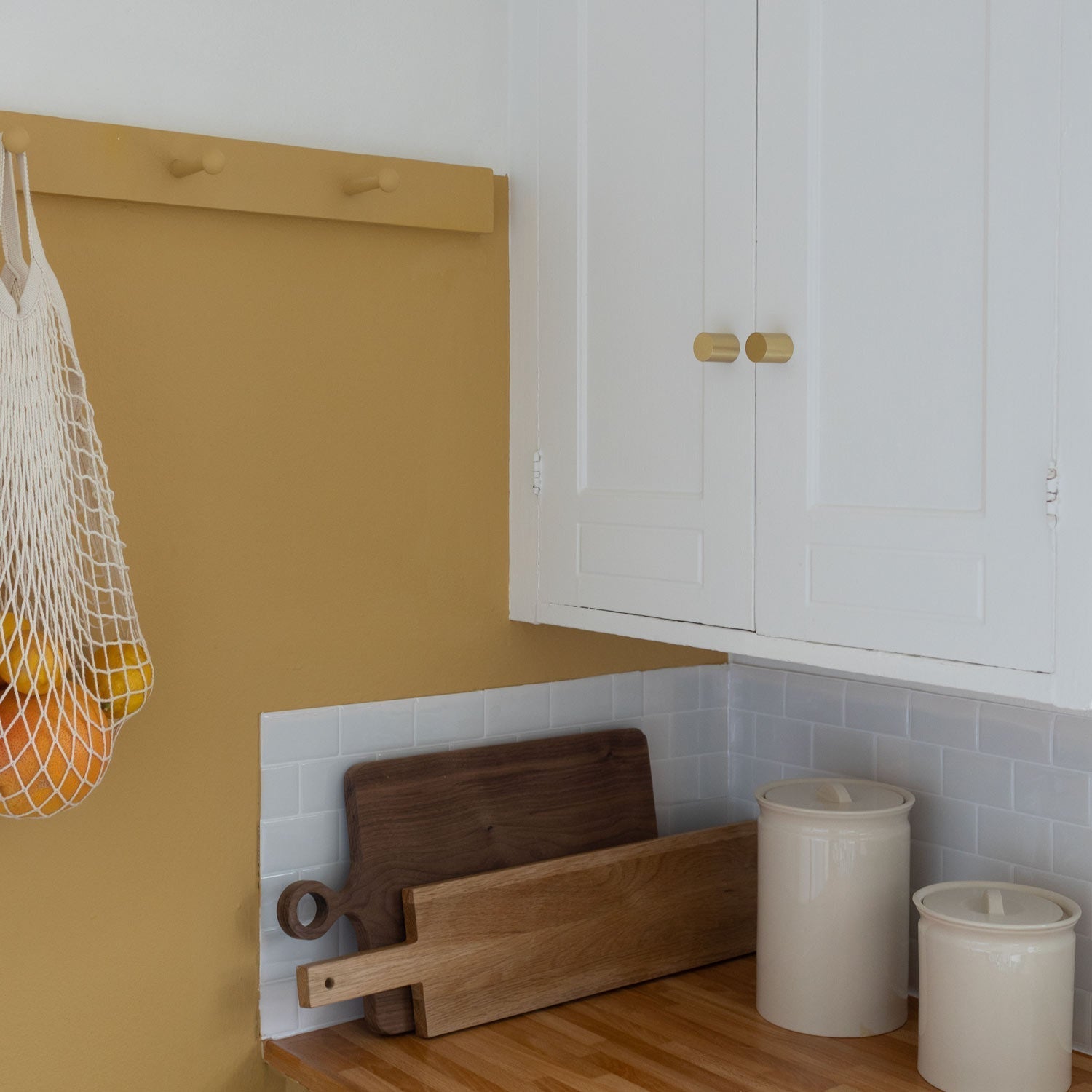 Front view of Cove Knob showcasing cylindrical brass-colored hardware on white cabinet doors in a kitchen