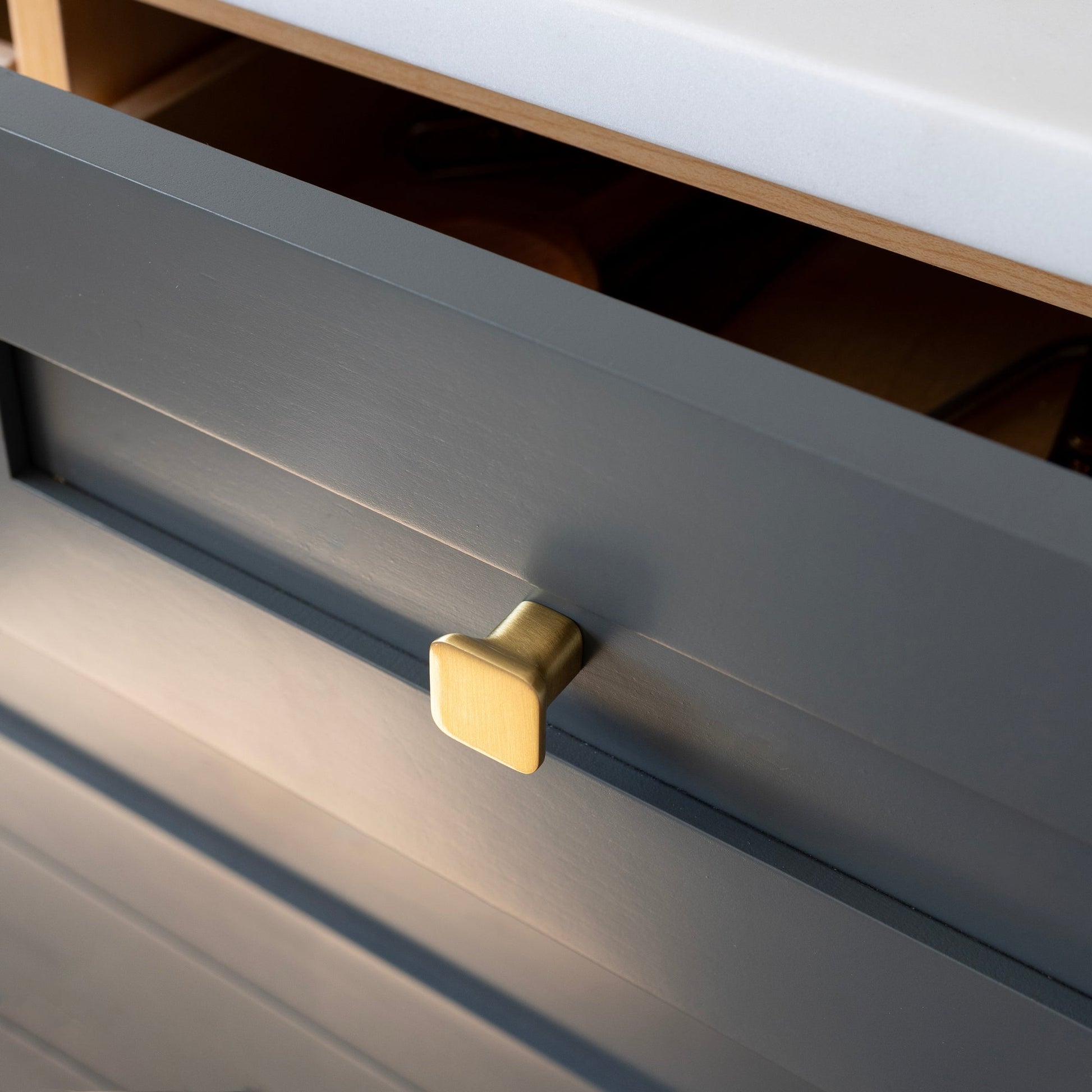 Close-up view of Cascade Knob showcasing its natural brass finish on a dark drawer front