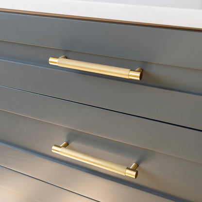 Angled view of the Knurled Pull showcasing its gold textured handle on gray drawers