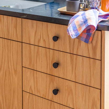 Close view of Edgecliff Knob showcasing its round black design installed on a wood cabinet beneath a kitchen countertop
