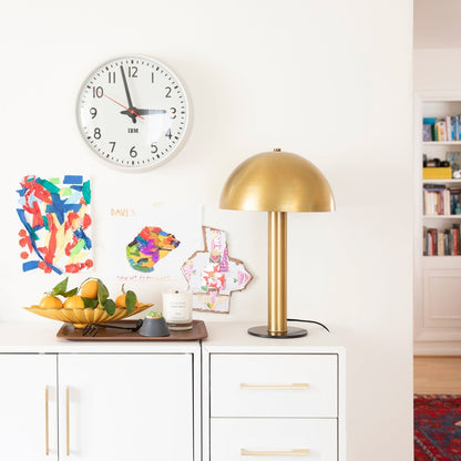 Natural brass Alberta Pulls installed on a white cabinet beside a brass table lamp