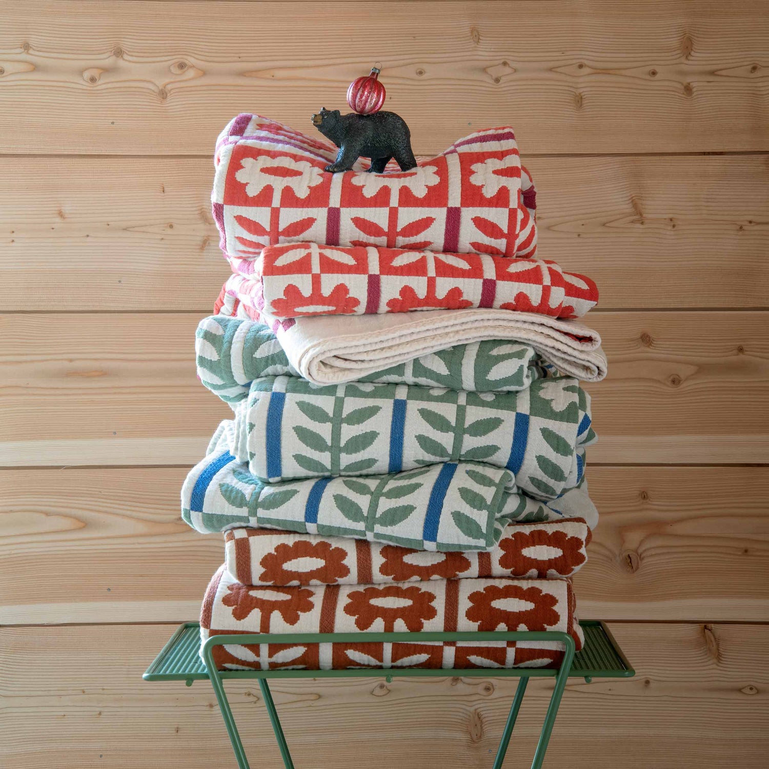 Front view of stacked Stillwater Floral Quilts showcasing multicolor botanical patterns on a green side table against wood paneling