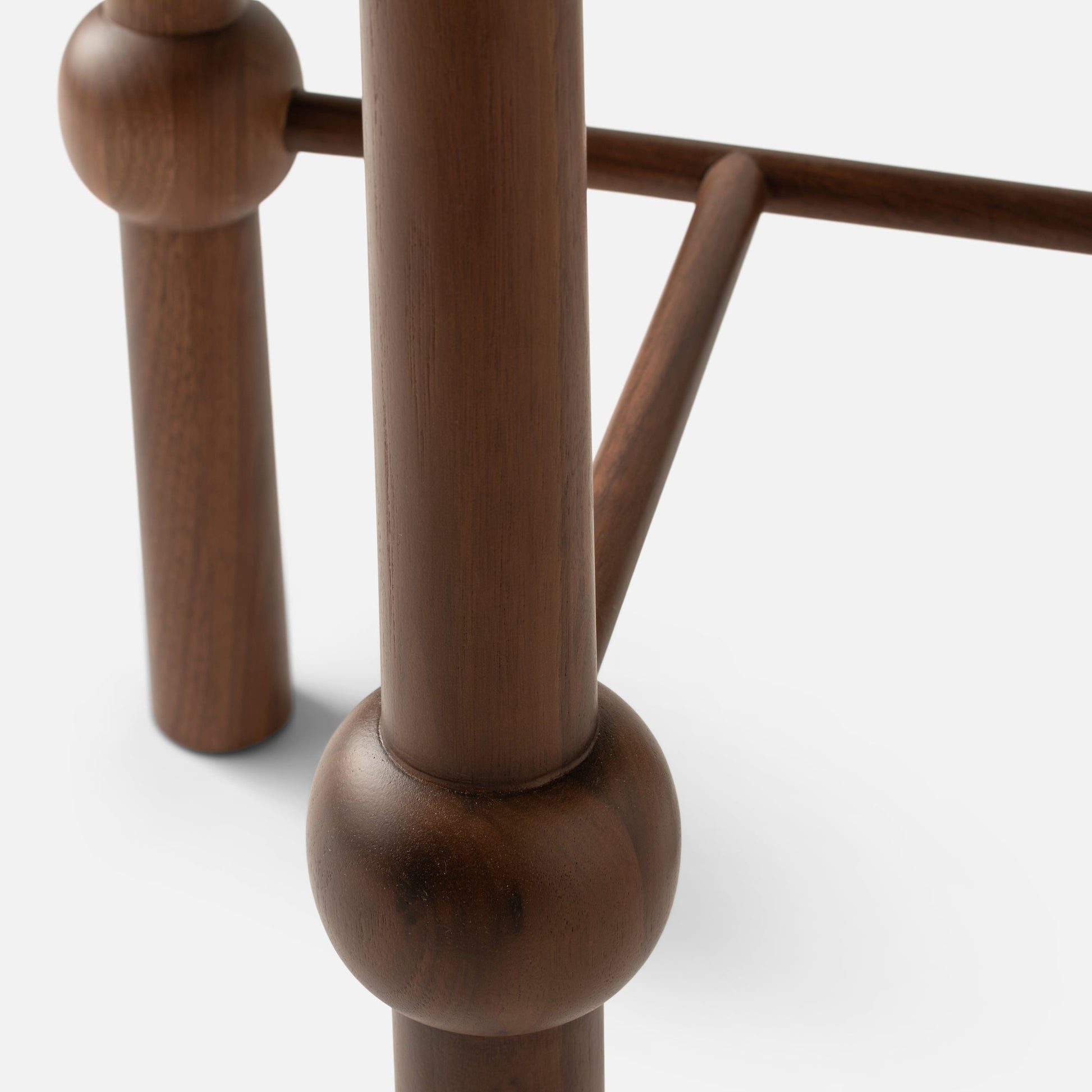 Close-up of Ann Occasional Table leg showing faceted walnut joint and round dowel stretcher on white background
