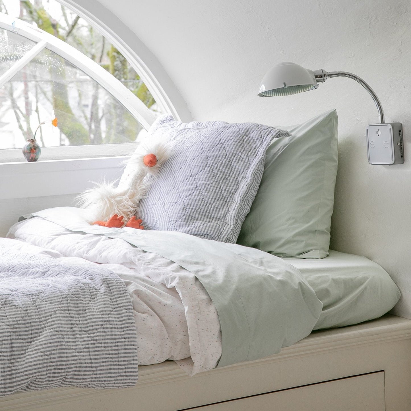 Angled view of Diamond Ticking Quilted Pillow Sham showing diamond quilted ticking pattern and subtle striped texture on a bed by an arched window