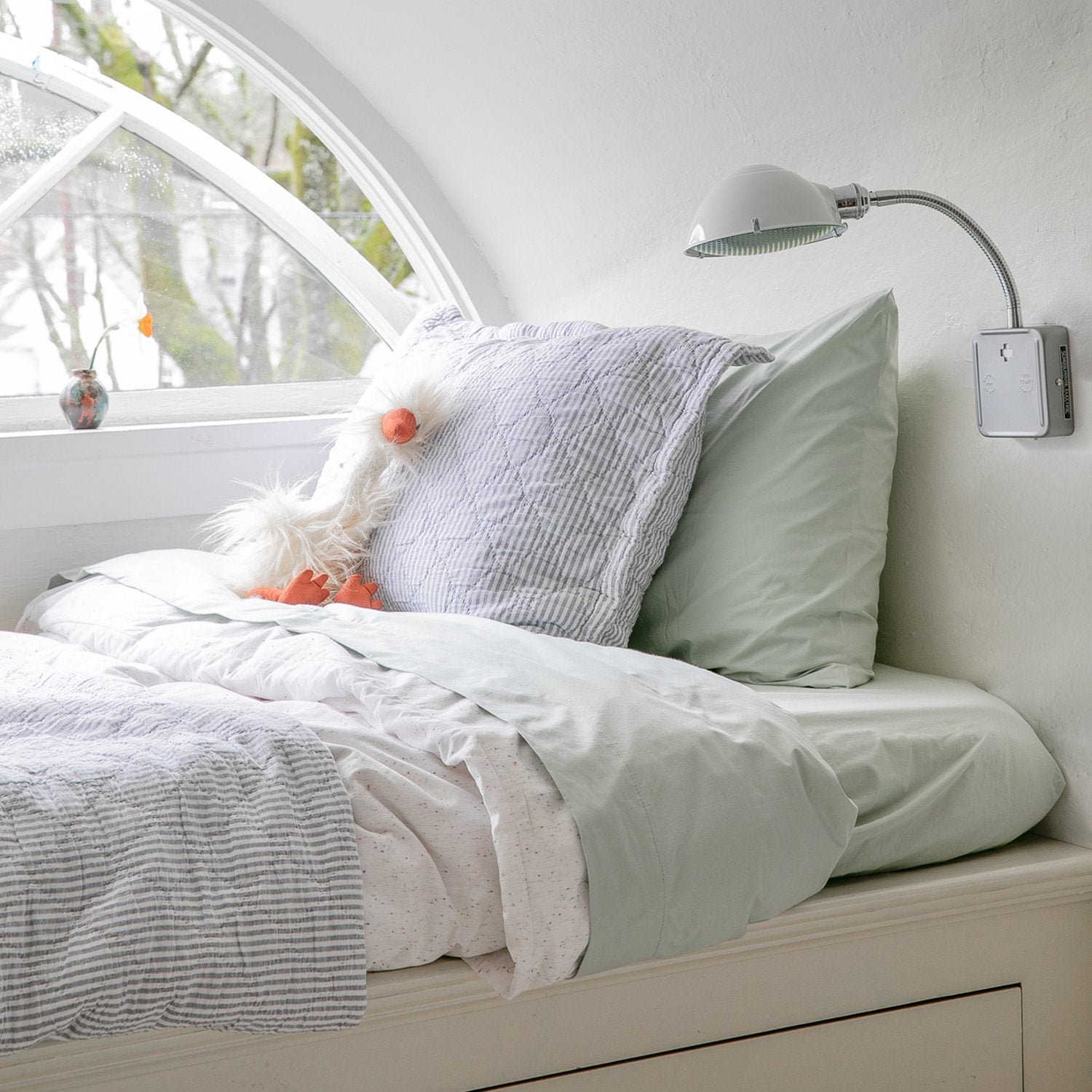 Angled view of Diamond Ticking Quilted Pillow Sham showing diamond quilted ticking pattern and subtle striped texture on a bed by an arched window