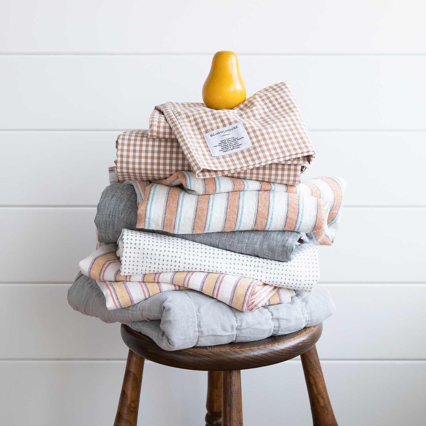 Stacked view of russet gingham pillowcase set (2) showing check pattern and Schoolhouse label on top of folded linens on a wooden stool