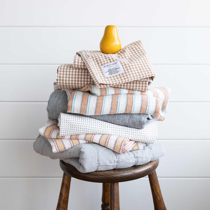 Stacked view of russet gingham pillowcase set (2) showing check pattern and Schoolhouse label on top of folded linens on a wooden stool