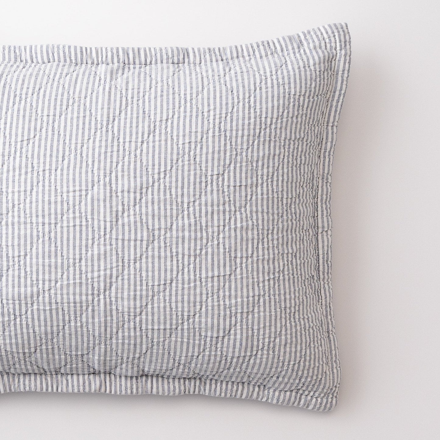 Close-up of Diamond Ticking Quilted Pillow Sham showing narrow blue and white ticking stripes and diamond quilting on a white background
